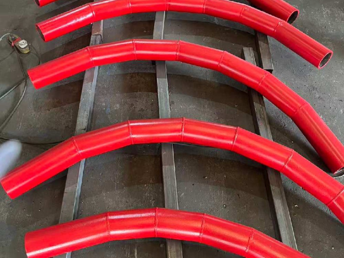Red wear-pipe bends resting on skids in the workshop